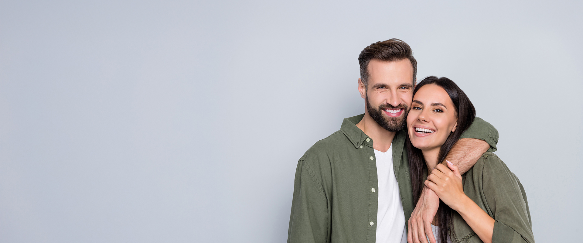 A man and woman hugging each other closely while posing for a photograph against a plain background.