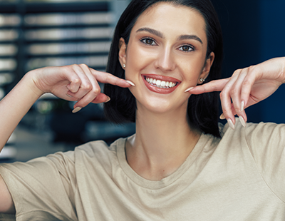A woman with a radiant smile, posing for a photograph while holding her hand near her mouth.