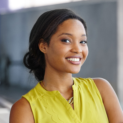 A woman with a radiant smile poses confidently against a backdrop of a building, exuding positivity and warmth.