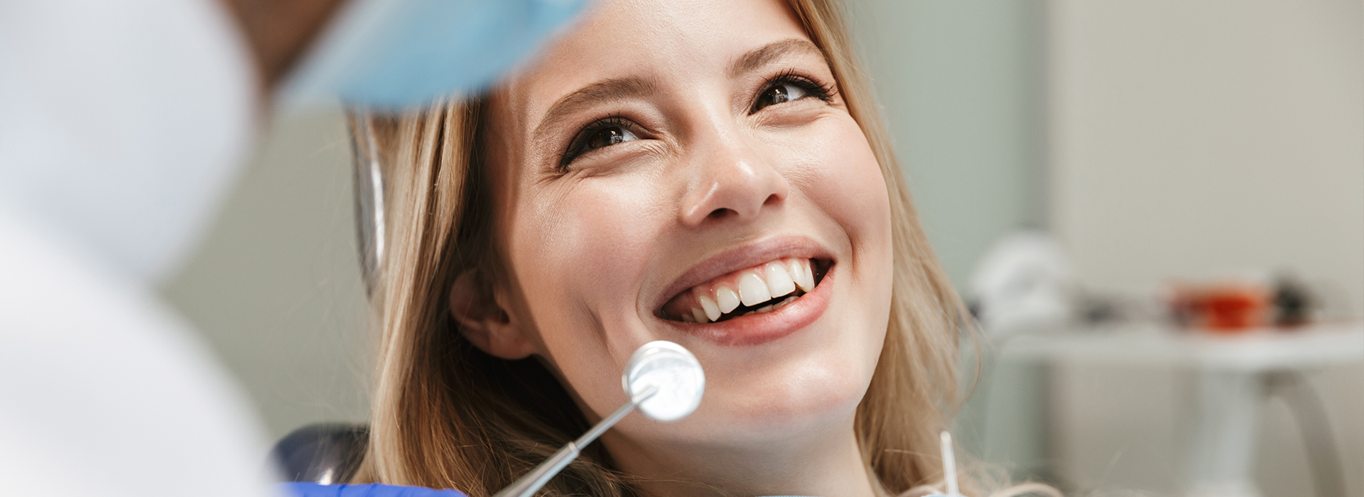 Woman with a bright smile sitting in front of dental equipment, likely at a dentist s office.