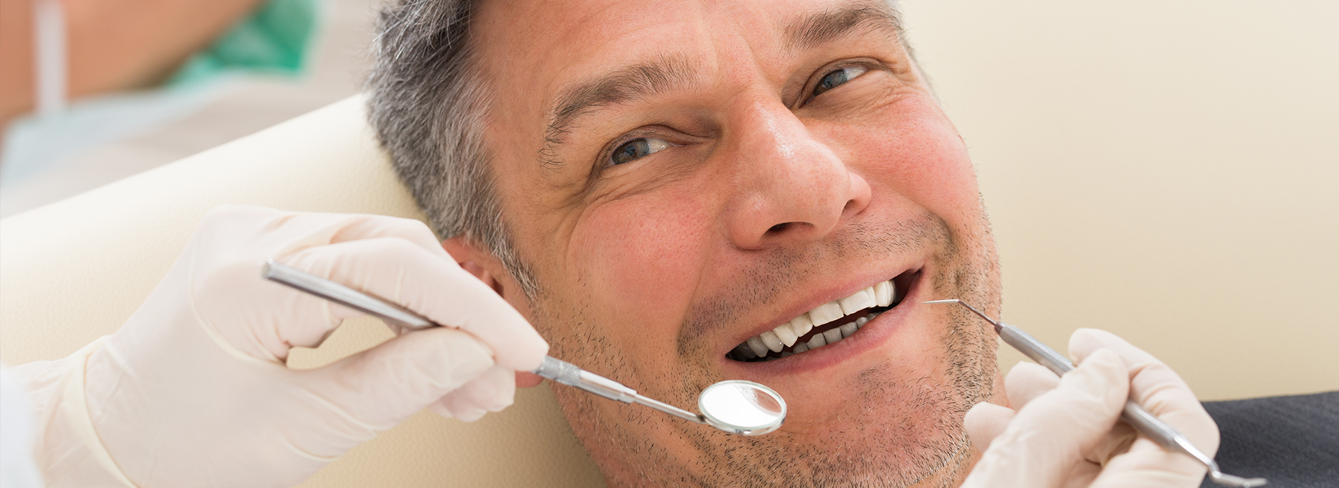 A man sitting in a dental chair receiving dental treatment with a smile on his face while wearing protective gloves.