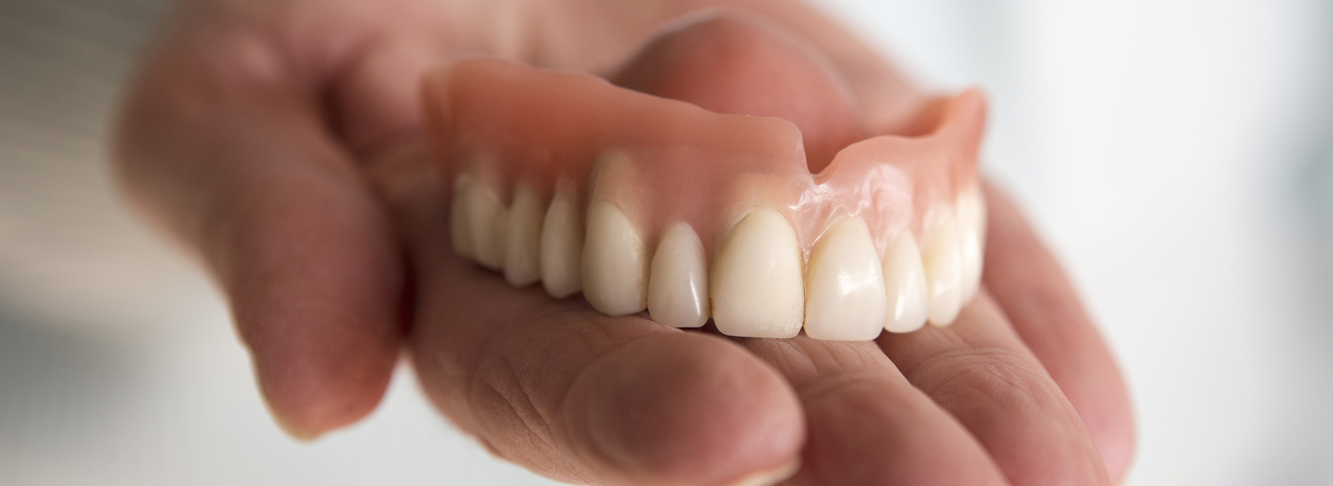 A hand holding a set of dentures with an artificial mouth showing a full set of teeth.