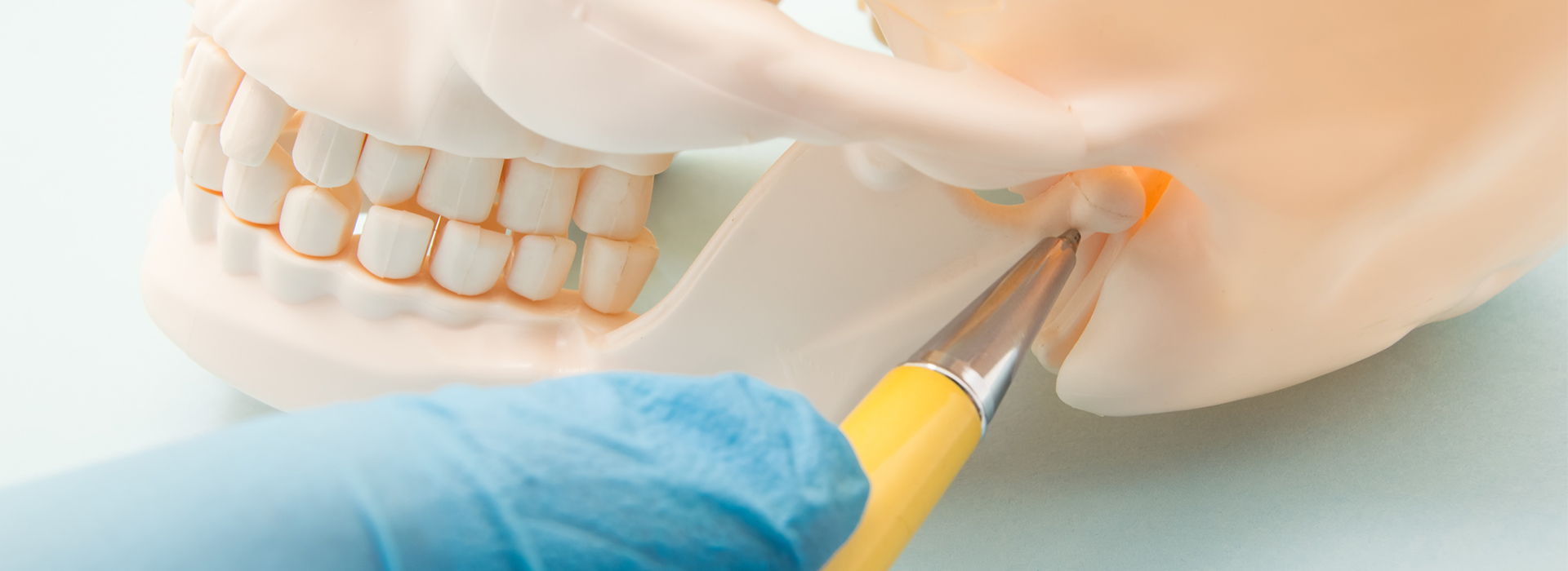 A close-up photograph of a dental implant procedure with a surgeon s hand holding a screwdriver over a plastic skull model, set against a blue background.