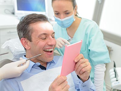 A man holding up a pink card with a joyful expression while seated in a dental chair, surrounded by dental professionals who are smiling and observing him.