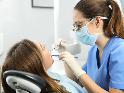 A dental professional, wearing gloves and a face mask, is performing oral care on a seated patient.