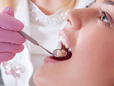 A dental professional is performing an oral examination on a patient s mouth using a mirror and a probe.