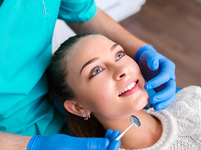 A dental hygienist performing a teeth cleaning procedure on a patient s mouth while wearing protective gloves and a face mask.