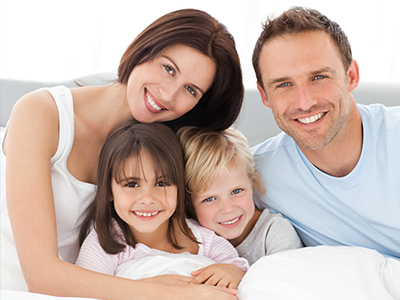 A family of four posing together on a bed with a white background.