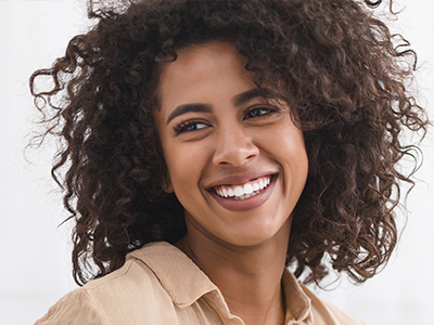 The image features a woman with curly hair smiling broadly at the camera, wearing a light-colored top.